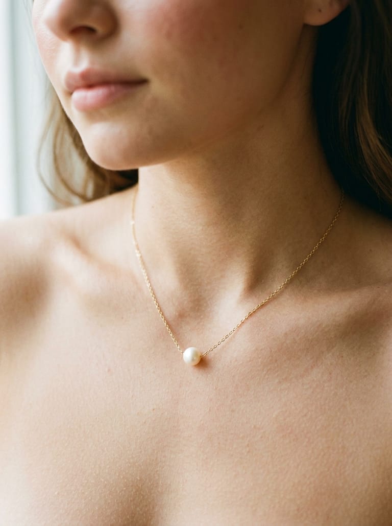 Close-up of a gold pearl pendant necklace resting on skin